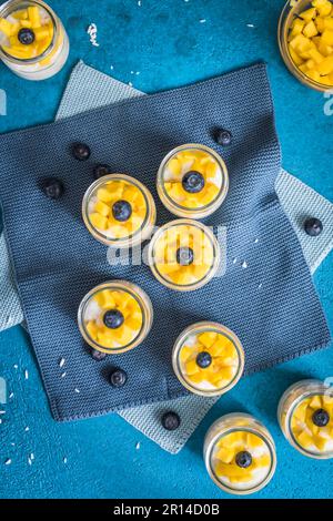 Budino di riso al cocco con mango in bicchieri da dessert su sfondo blu, verticale Foto Stock