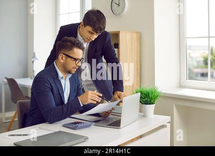 Direttore finanziario maschile che fornisce indicazioni al suo assistente mentre lavora al rapporto finanziario. Foto Stock