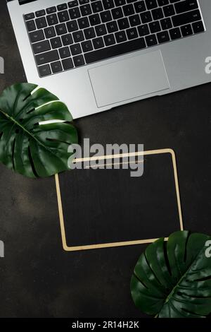 Area di lavoro con lavagna a clip vuota e computer portatile su sfondo nero. Scrivania da ufficio con vista dall'alto. Foto Stock