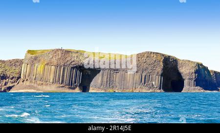 Turisti che camminano sulla famosa isola di Staffa, composta da colonne di basalto esagonale scuro, Ebridi interne, Scozia. Foto Stock