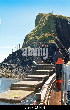 Isola di Staffa, Ebridi interne, Scozia - 14 giugno 2015: Il molo di atterraggio e ripidi scalini sulle scogliere, un traghetto che si affianca. Foto Stock