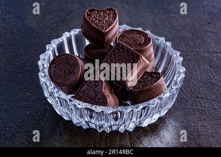 Cioccolatini su vassoio di vetro intagliato, fotografati su sfondo scuro con fagioli di cacao. Foto Stock