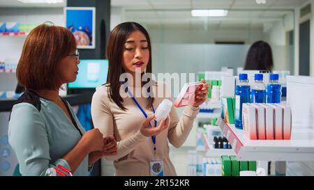 Assistente di farmacia che spiega le vitamine al cliente femminile, parlando in farmacia farmaceutica. Giovane donna aiutare il cliente con integratori medici e prodotti per la salute, pillole pacchetti. Foto Stock