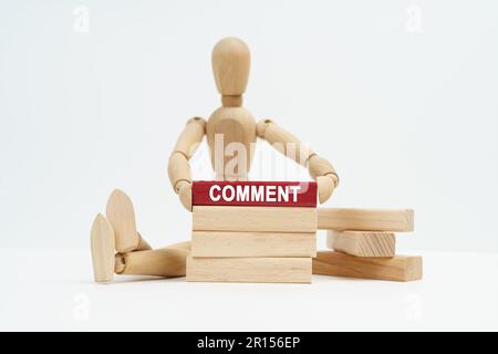 Concetto aziendale. Su una superficie bianca siede un uomo di legno nelle sue mani un blocco con l'iscrizione - COMMENTO Foto Stock