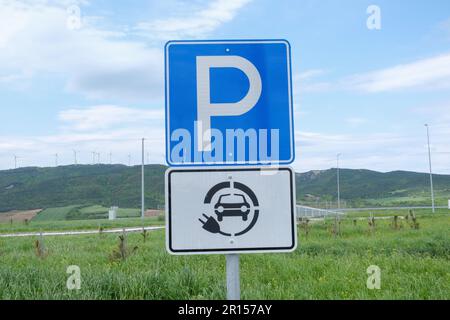 Cartello dei punti di ricarica per auto elettriche e parcheggi con area verde e sfondo cielo. Foto Stock