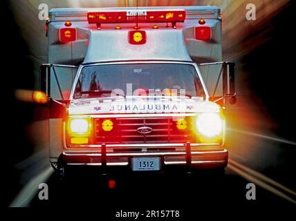 Immagine di sfocatura in movimento di un'ambulanza in rapido movimento con luci lampeggianti che si precipitano direttamente verso la telecamera su un'autostrada a due corsie Foto Stock