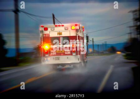 Ambulanza che corre lungo una strada rurale piovosa Foto Stock