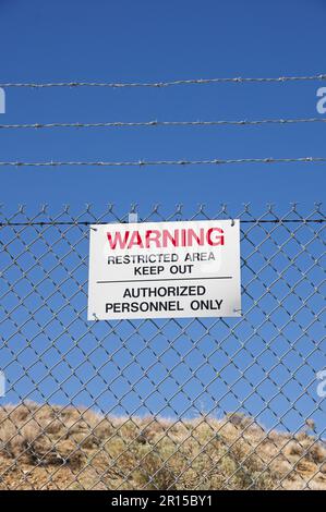 avvertenza area riservata tenere fuori il personale autorizzato firmare solo su una recinzione di maglia della catena di filo spinato con cielo blu nel deserto Foto Stock