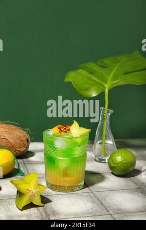 Fresco cocktail estivo con carambola e fiore su tavolo in piastrelle vicino al muro verde Foto Stock