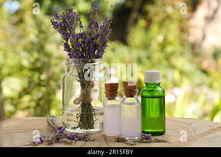 Bellissimi fiori di lavanda e bottiglie di olio essenziale su ceppo di legno Foto Stock