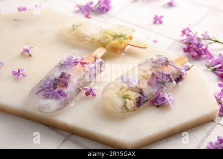 Tavola con bellissimi popsicles floreali e fiori di lilla su sfondo piastrelle chiaro Foto Stock