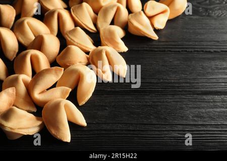 Biscotti gustosi della fortuna con le previsioni sul tavolo nero di legno, spazio per il testo Foto Stock