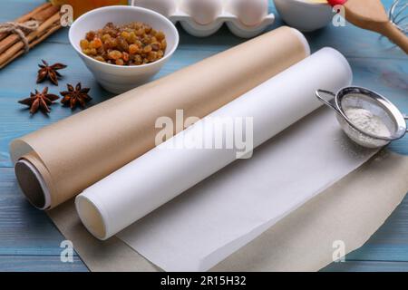 Rotoli di carta da forno, diversi ingredienti e utensili da cucina su tavola di legno azzurro Foto Stock