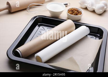 Teglia da forno con rotoli di carta pergamena, ingredienti diversi e utensili da cucina su tavolo di legno Foto Stock