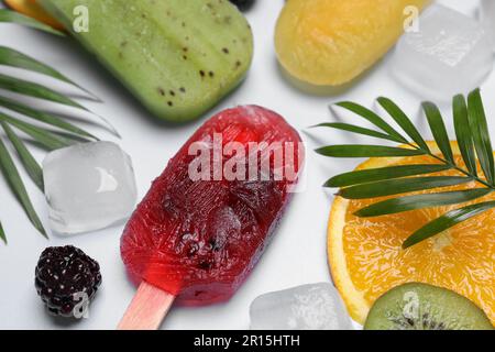 Deliziosi popsicli, frutta fresca e cubetti di ghiaccio su sfondo chiaro, primo piano Foto Stock