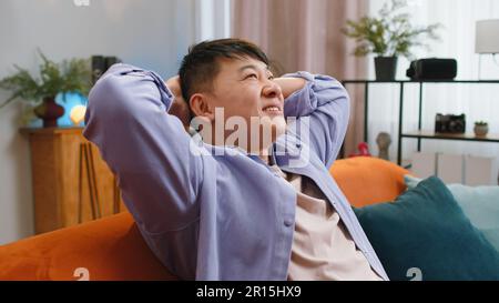 Ritratto di uomo asiatico stanco godere di rilassarsi sul divano a casa in camera. Felice ragazzo cinese sdraiato sul divano riposo napping dopo dura giornata di lavoro, chiuso gli occhi, mettere le mani dietro la testa, senza stress Foto Stock