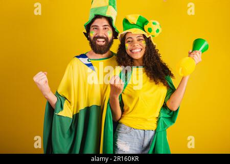 coppia di tifosi brasiliani di calcio, vestita nei colori della nazione, donna nera, uomo caucasico. utilizzo della bandiera e degli accessori Foto Stock