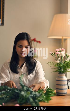 Ritratto di una bella felice giovane donna asiatica che organizza fiori nel suo salotto minimo. Concetto di svago e hobby Foto Stock