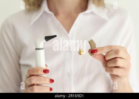 La donna tiene in studio un otoscopio digitale e un apparecchio acustico Foto Stock