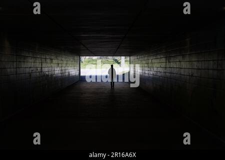 Silhouette di una persona a piedi attraverso un sottopassaggio buio che simboleggia la luce alla fine del tunnel Foto Stock