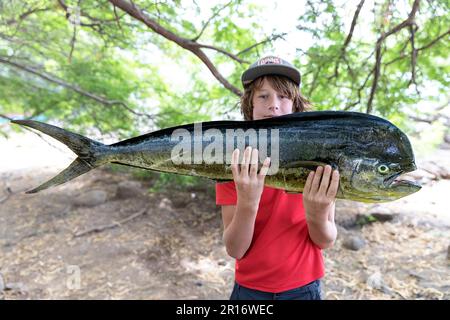 Teenager turistico che tiene un bel pesce dorado all'ombra di un albero in un piccolo villaggio di pescatori di tarrafal de monte tigo, santo antao, cabo verde Foto Stock