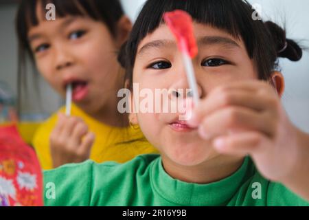 Due ragazze cute felici che mangiano i lollipops. Ragazzo divertente con caramelle lecca lecca. Bambino che mangia dolci. Foto Stock