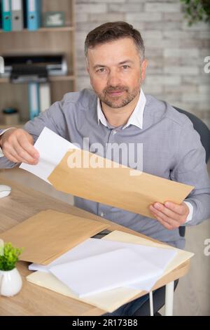 uomo d'affari che legge una lettera seduto in una scrivania in ufficio Foto Stock