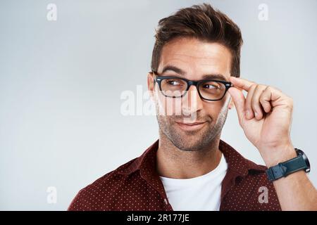 Regolazione delle lenti. Studio shot di un giovane uomo allegro che indossa occhiali e sorridente luminoso mentre si alza su uno sfondo grigio. Foto Stock