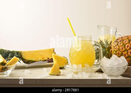 Bicchiere pieno di ananas bevanda con ghiaccio sul tavolo con ghiaccio tritato e frutta e sfondo isolato. Vista frontale. Composizione orizzontale. Foto Stock