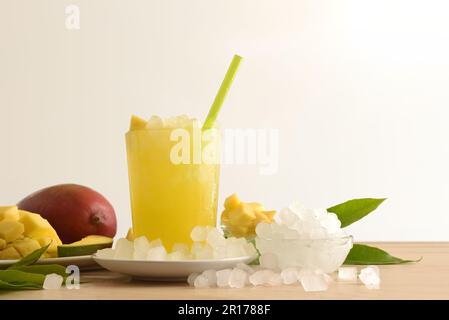 Particolare della bevanda di mango con molto ghiaccio su una panca di legno della cucina con la frutta e una ciotola con il ghiaccio intorno esso fondo isolato. Vista frontale. Orizzontale Foto Stock