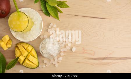 Sfondo con particolare di bevanda mango con un sacco di ghiaccio su una panca di legno da cucina con frutta decorata e una ciotola con ghiaccio intorno ad essa. Vista dall'alto. Horizo Foto Stock