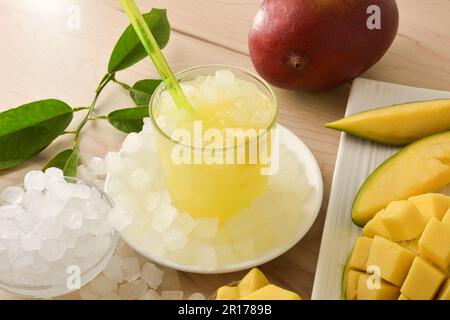 Particolare bicchiere con bevanda fredda di mango su piatto con ghiaccio e frutta intorno. Vista rialzata. Composizione orizzontale. Foto Stock