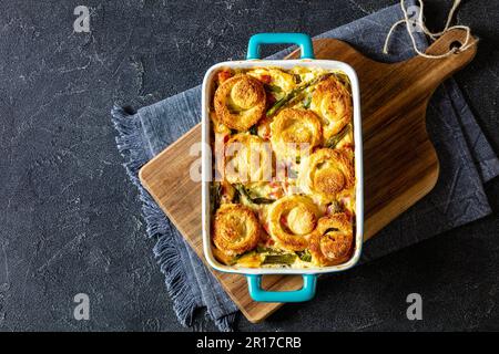 casseruola di prosciutto di asparagi sormontata con ciambelle di pan di spagna in teglia da forno su tavolo di cemento, vista orizzontale dall'alto, giacitura piatta Foto Stock