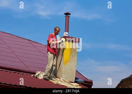 opera di un pittore sul tetto, un uomo dipinge un camino di colore giallo pennello Foto Stock