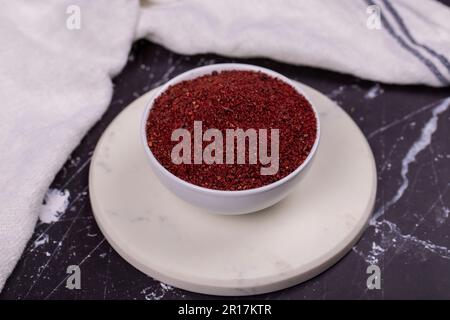 Sumac su sfondo scuro. Spezie in polvere di Sumac rosso macinato essiccato in recipiente di legno Foto Stock