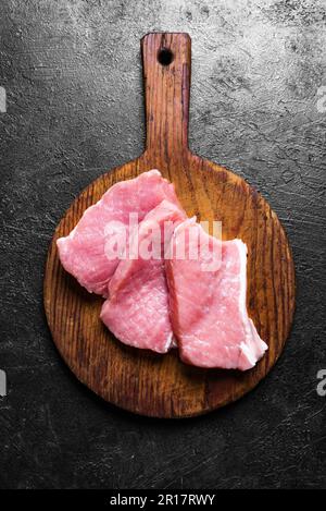 Fette di carne di maiale cruda sul tagliere, vista dall'alto. Pezzi di lombo di maiale. Foto Stock