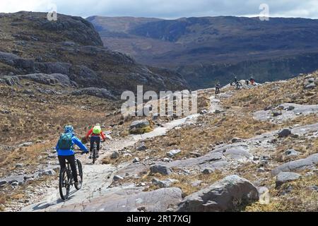 Scottich Highlands, Coulin Estate. Gli appassionati di mountain bike scendono da Coire Lair verso Loch Dughaill, vicino a Lochcarron. Cime di Sgurr na Feartaig oltre. Foto Stock