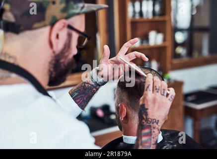 Il dettaglio fa la differenza. un bel giovane barbiere che dona al cliente un taglio di capelli all'interno del suo barbiere. Foto Stock