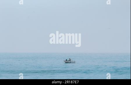 Due pescatori su una piccola barca bianca navigando nel vasto oceano aperto in una giornata di nebbia Foto Stock