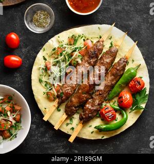Kebab con verdure fresche su pane piatto su fondo di pietra nera. Vista dall'alto, disposizione piatta Foto Stock