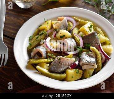 Insalata di aringhe con patate bollite, cetrioli sottaceto e cipolla rossa su piatto su sfondo di legno. Vista ravvicinata Foto Stock