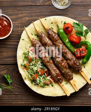 Kebab con verdure fresche su pane piatto su sfondo di legno. Vista dall'alto, disposizione piatta Foto Stock