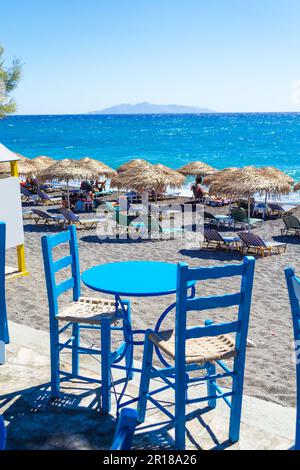 Settembre 5th 2013:Vintage tavolo blu con due sedie che si affaccia sulla spiaggia di Black quarz, ANAFI isola in Distance.Kamari, Santorini, Grecia Foto Stock