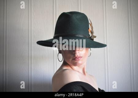 Una femmina bianca che indossava un grande brimmed, stile fedora aveva impostato su uno sfondo grigio pallido Foto Stock