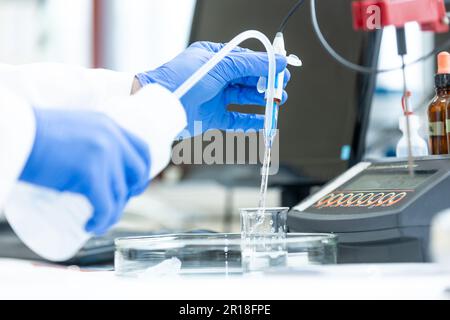 Tecnico di laboratorio con elettrodo in vetro per la misurazione del pH della soluzione mediante pHmetro, laboratorio di analisi o elettrochimica, laboratorio Foto Stock