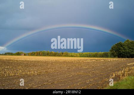 Una vista mozzafiato di un doppio arcobaleno nel cielo su un campo appena raccolto durante una giornata tempestosa Foto Stock