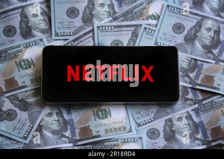 Logo Netflix visualizzato sullo smartphone in cima a una pila di soldi. Foto Stock