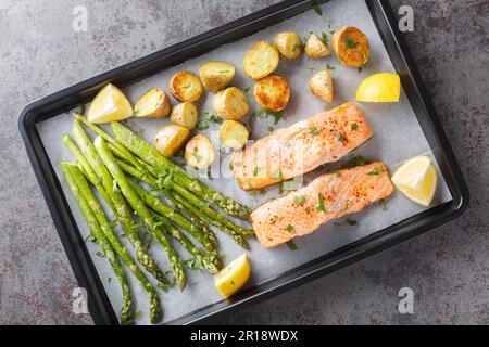 Delizioso filetto di salmone sano cotto con asparagi e patate novelle primo piano in una teglia da forno sul tavolo. inclinazione orizzontale superiore dall'alto Foto Stock