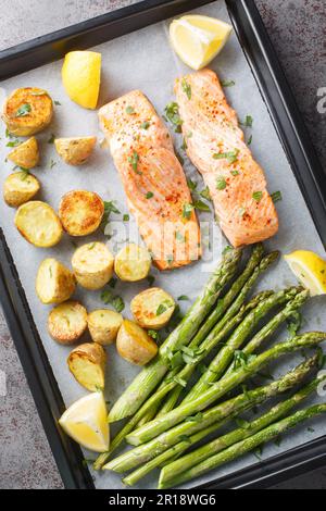 Filetto di salmone fatto in casa cotto con asparagi e patate novelle con erbe e limone primo piano in una teglia da forno sul tavolo. verticale dall'alto Foto Stock