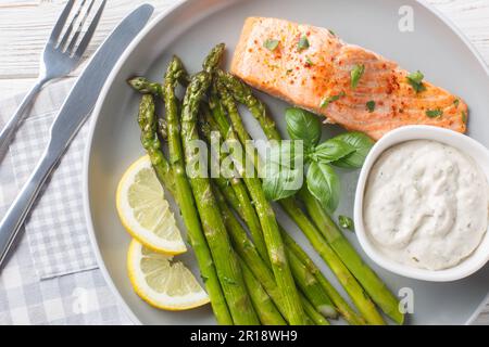 Filetto di salmone selvatico con asparagi servito con salsa tartara e primo piano al limone in un piatto sul tavolo. Inclinazione orizzontale superiore dall'alto Foto Stock